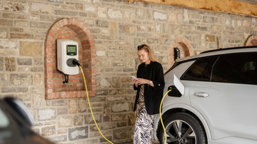 Frau schaut aufs Handy beim Laden eines E-Autos